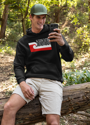 Maori tane sitting on a fallen tree trunk in the nagger forest, wearing a custom pepeha hoodie by Mana Ake Kaupapa Creative